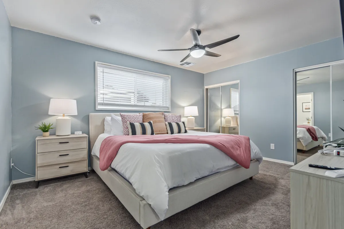 A serene bedroom featuring a large, inviting bed flanked by nightstands, a mirrored wardrobe, and a bright window allowing natural light to stream in. The room balances soft textures with understated décor, creating a restful ambiance.
