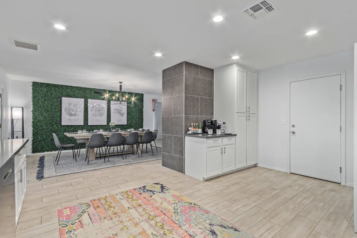 This image presents a sophisticated dining table with chairs, a striking green wall with artwork, and a view into the kitchen area with stylish cabinetry. The setup demonstrates the dining area’s capacity and its adjacency to the kitchen, enhancing the sense of flow.