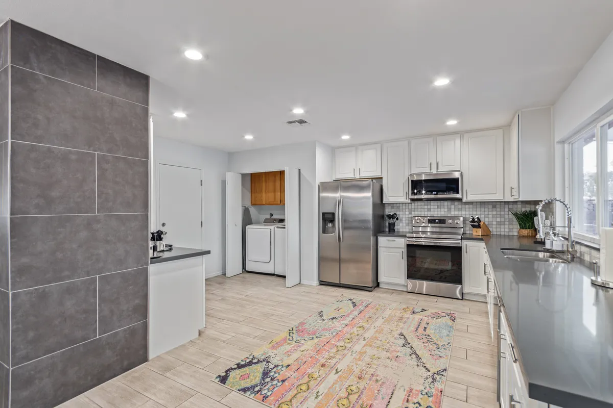 Featuring a modern kitchen with stainless steel appliances, a decorative rug, and a spacious kitchen island, this scene illustrates a fully stocked, functional cooking space. The layout is perfect for preparing meals and entertaining, and hints at the pass-through bar feature.