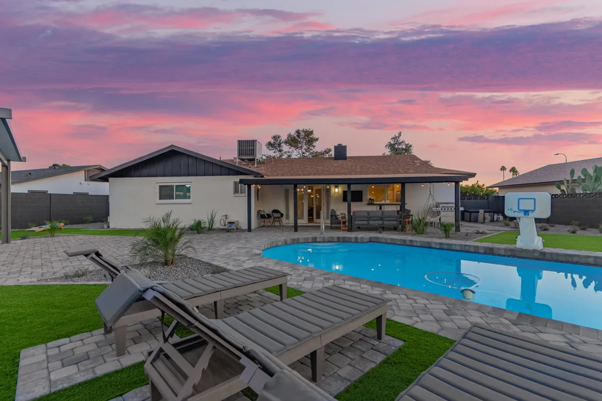 A view of the swimming pool surrounded by lounge chairs, set against a vibrant sunset sky. The area is designed for both fun and relaxation, perfect for families to enjoy together. The image captures the essence of outdoor family activities such as swimming and entertaining, with ample space for children to play safely under adult supervision.