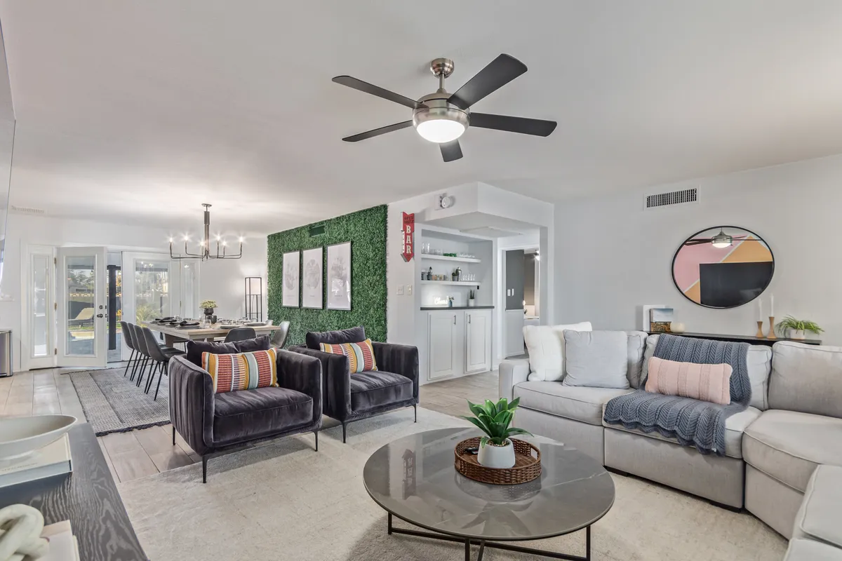 This image features a spacious, comfortable sectional sofa, stylish armchairs, and a dining area with an elegant chandelier and a green accent wall. The harmonious arrangement of seating closely aligns with the open-plan living and dining concept described. The inviting decor and the warm, contemporary mood emphasize areas for both relaxation and togetherness.