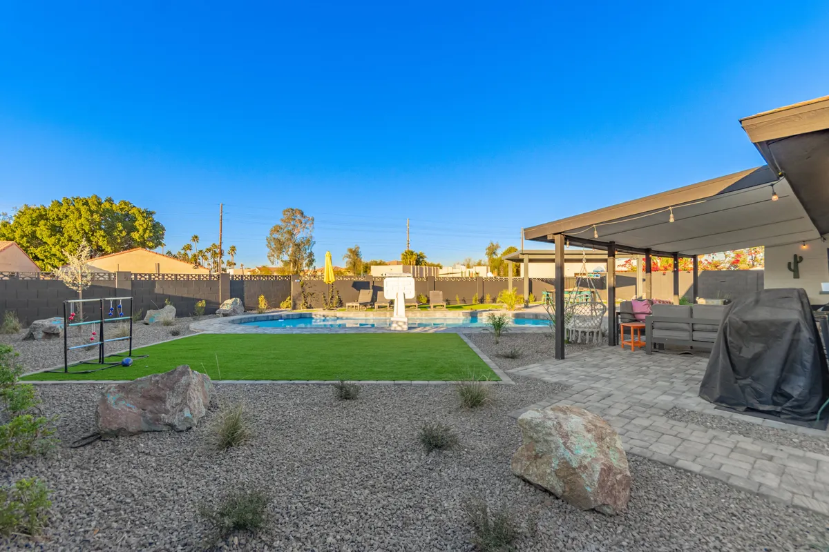 A spacious backyard with a swimming pool, lawn area, outdoor seating, and a visible play area. The space is ideal for both relaxation and play, catering to all ages with areas for swimming, lounging, and children's games. The image radiates a joyful and inviting atmosphere.