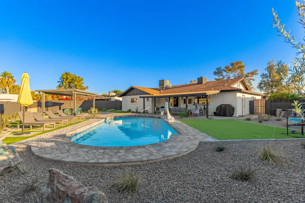This exterior image features a sparkling swimming pool surrounded by lounge chairs, a patio area, and an outdoor grill, all set amidst a lush landscaped garden. The scene is lively and social, hinting at both leisurely swims and opportunities for group gatherings or solo relaxing after a day of work.