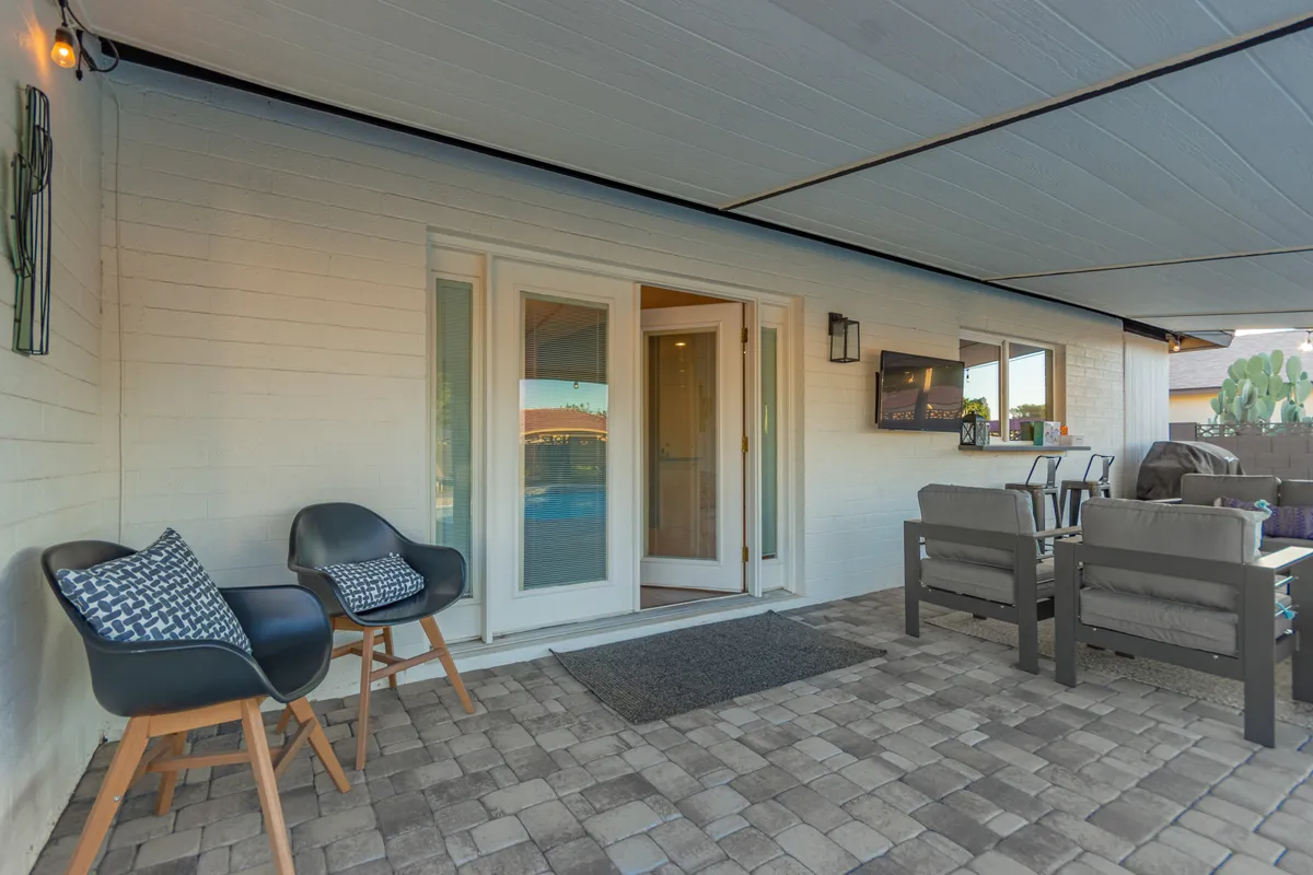 An inviting exterior seating area with a covered patio, double doors leading to the interior, and a small wall-mounted TV. The space is ideal for morning coffee or catching a game with friends, offering a smooth transition between indoor comfort and outdoor enjoyment.
