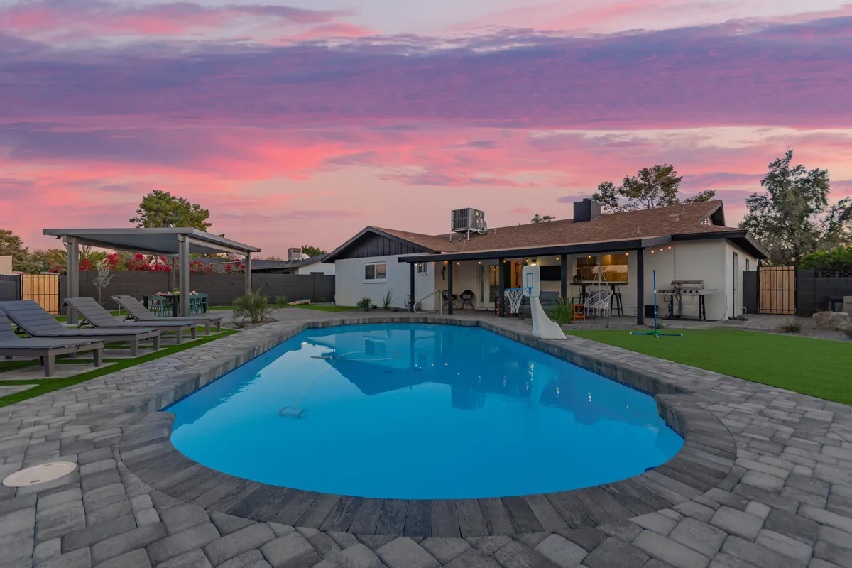 An expansive exterior scene featuring a swimming pool, outdoor seating area, and a colorful sunset sky. The area is set up for socializing, dining, or relaxing by the pool, ideal for families to gather after a day of exploring local attractions.